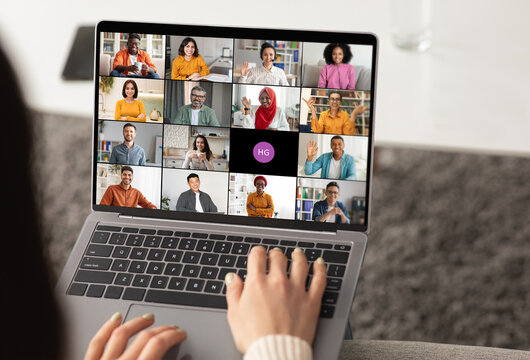 Woman using a laptop to participate in an online video chat meeting. The screen displays several participants in a grid format, showcasing a diverse group of people.