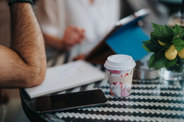 A casual business meeting in a coffee shop, featuring documents, a phone, and a coffee cup on the table.