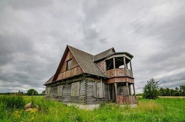 Old wooden farmhouse in the countryside with storm clouds in the sky. There is a short grass meadow around the house.