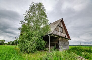Old wooden farmhouse in the countryside with storm clouds in the sky. There is a short grass meadow around the house.