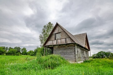 Old wooden farmhouse in the countryside with storm clouds in the sky. There is a short grass meadow around the house.