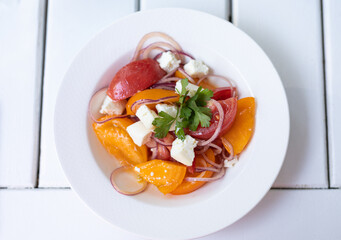 salad with yellow and red tomatoes, cheese and onions in a white plate on the table