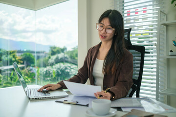 Asian businesswoman in eyeglasses working with financial reports at modern office.