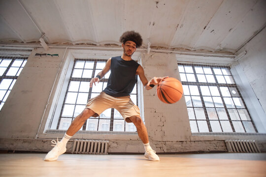 Wide angle action shot of African American basketball player dribbling ball while practicing in indoor gym copy space