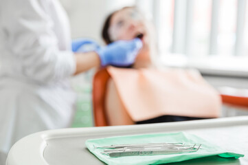 Obraz premium Dentist Treating Patient with Tools. Dentist in gloves treating a patient in a dental chair, with focus on dental tools in the foreground.