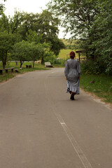 Young woman in old fashioned dress walking by the road from back