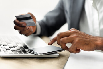A person holds a credit card in one hand and uses a smartphone with the other hand, likely to make an online purchase.