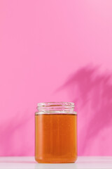 A jar of honey rests on a pink background, symbolizing the sweetness and purity of nature