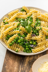 Tasty pasta with green peas and basil on white marble table