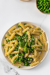 Vegetarian pasta with boiled green peas and basil on plate