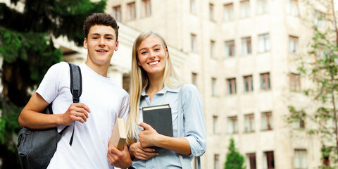 Obraz premium Happy university students holding books and smiling to camera in front of university