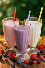 set of strawberry, banana and blueberry flavor milkshakes or smoothie in glasses on table outdoors