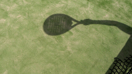The shadow of a hand with a racket on a green tennis court.Tennis or padel