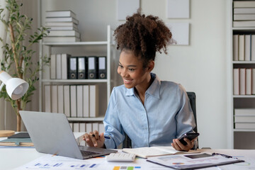 Young businesswoman working in office using laptop and holding smartphone