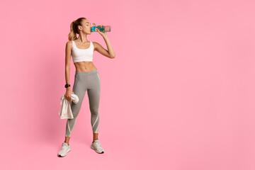 Slim Young Lady Drinking Water Holding Towel Standing Over Yellow Background In Studio. Workout Break.