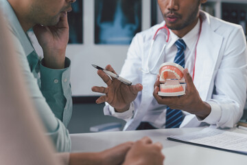 Fototapeta premium Dentist explaining teeth problem holding jaw model during medical consultation