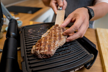Chef at the kitchen preparing beef steaks on the home electric grill