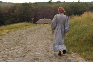 Brunette woman in vintage dress walking by a countryside brick road from the back