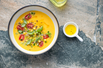 Bowl of sweet corn and yellow tomatoes gazpacho, above view on a grey and beige granite background,...