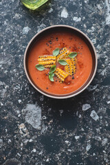 Bowl with roasted tomato and corn soup, top view on a dark-brown granite background, vertical shot, copy space