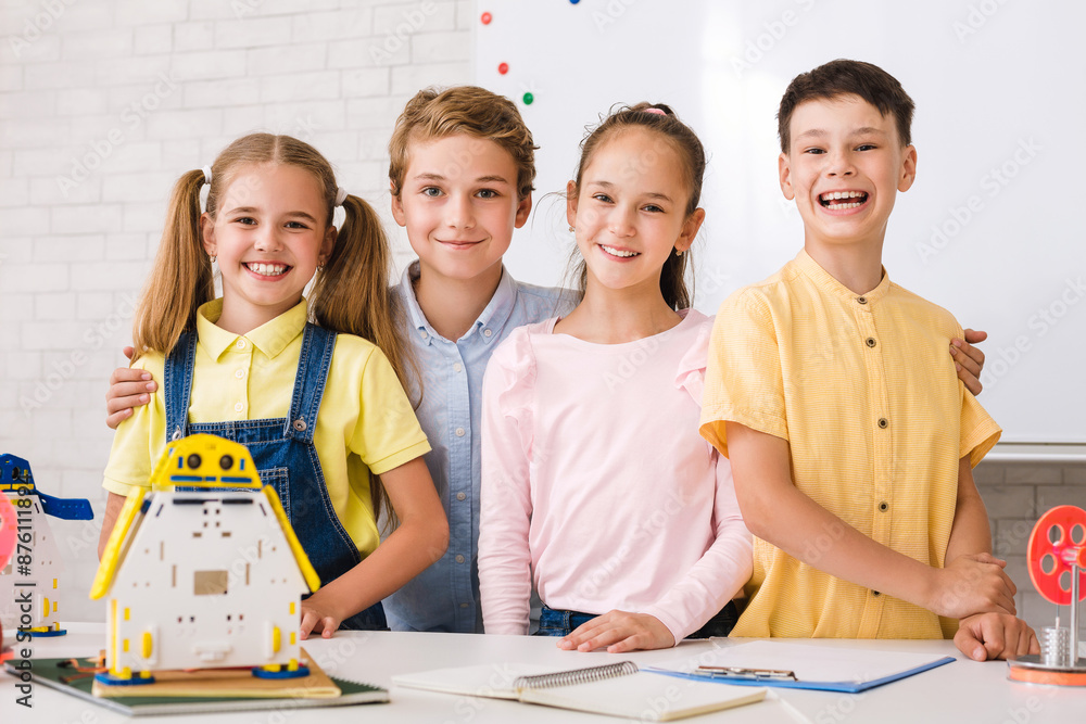 Aufkleber A group of four students are working on a robotics project in a classroom. They are smiling and appear to be enjoying themselves. There are various robot models on the table in front of them.