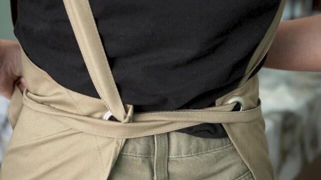 Women's hands tie an apron behind their back. Close up