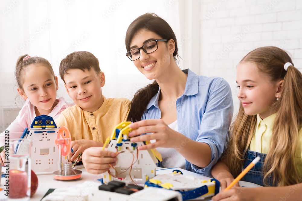 Poster A teacher is assisting a group of students as they build robot models during a STEM classroom lesson. The students appear engaged and excited as they work on their projects
