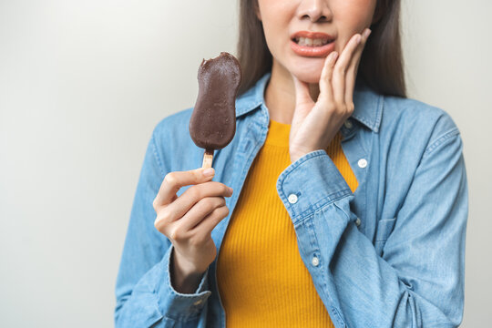 Face expression suffering from sensitive teeth and cold, asian young woman touching cheek, hurt or pain eating ice cream with chocolate. Toothache molar tooth, dental problem isolated on background.