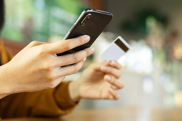 Close-up female hands holding credit card and smartphone, young woman paying online, using banking service, entering information, shopping, ordering in internet store, doing secure payment