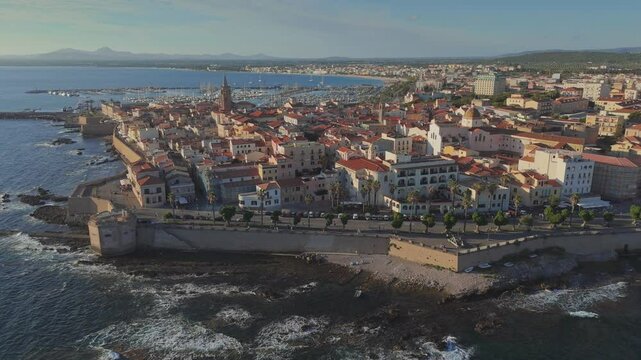 Flying around Alghero old town, Sardinia, Italy. Aerial shot of ancient Italian city and harbor at sunset