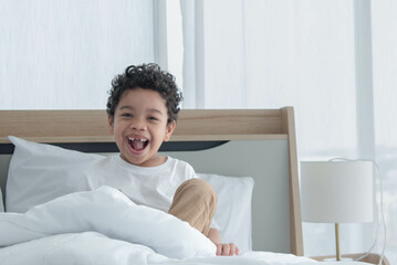 Asian boy smiles toothlessly lying on the bed under the blanket She is having fun posing for pictures
