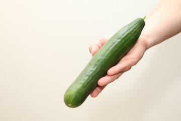 A Caucasian man holds a green long cucumber in a hand - white background