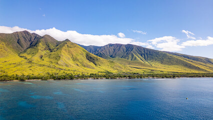 Aerial view of green volcanic and mountainous landscape meeting the bright blue coastline and shallow waters of island of Maui, Hawaii.  © James
