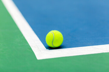 Tennis Ball on a Court Near the Baseline. A close-up shot of a bright yellow tennis ball resting on...