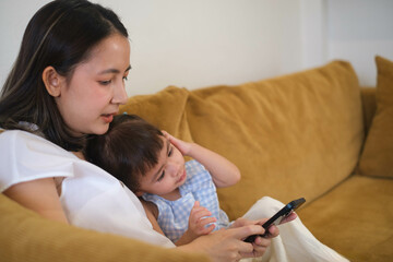 Mother and child sitting on a couch, bonding over a smartphone, enjoying quality time together, and sharing a moment of connection and love.