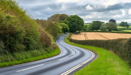 Fototapeta premium Winding curvy rural road with light trail from headlights leading through British countryside.