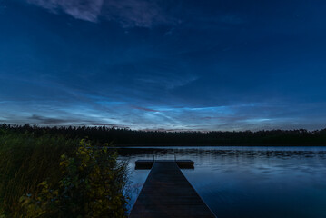 Noctilucent clouds over the forest lake in Latvia on July night