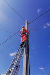 Electrician for high-speed cable Internet networks works at height on elongated stepladder leaning...