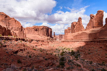 Breathtaking view of the Park Avenue area in Arches National Park, Utah, USA. Majestic red rock formations under a bright, partly cloudy sky. Perfect for travel, nature, and adventure themes.