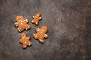 Four gingerbread men of different sizes on a dark rustic background, top view, flat lay, copy space.