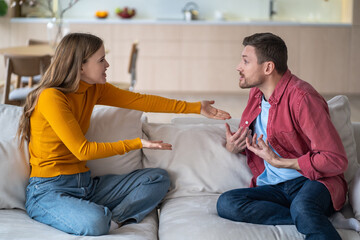 Married couple spouses quarrel, squabbling, fighting, vigorously gesticulating while sitting on couch. Aggressive wife blaming husband making excuses. Guy and girl violently discussing acute issue.