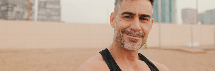 Close up, middle aged athletic man smiling and looking at camera while standing on the beach