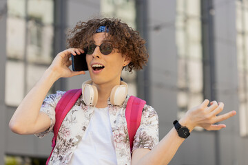 Happy young Caucasian man tourist having remote conversation communicate speaking by smartphone with friend, talking on phone unexpected good news gossip in urban city street. Town lifestyles outdoor.