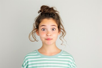 Young girl with surprised expression, wearing a striped shirt and messy bun hairstyle, looking directly at the camera.