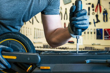 Repairing an electric scooter in a workshop. A close-up shot of a master disassembling a scooter with an electric screwdriver. © Konstantin