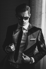 Obraz premium A man in a suit and sunglasses stands in a darkened room, his hand resting on his jacket lapel