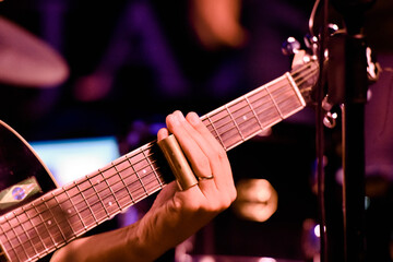 Details of the left hand of a blues guitarist with a metal slide on his pinky finger. Selective focus.
