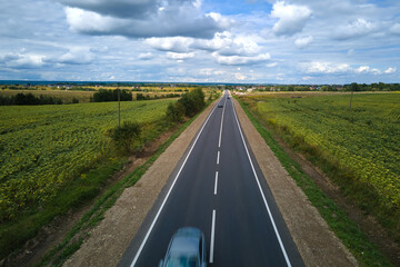 Aerial view of intercity road between green agricultural fields with fast driving cars. Top view from drone of highway traffic