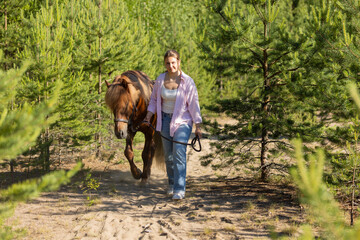 Woman with Icelandic horse between pines at summer evening