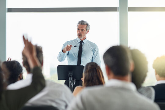 Podium, mature man and question in seminar, speaker and audience in event, training and presentation in boardroom. Workshop, speech and talking in conference, entrepreneurship and masterclass